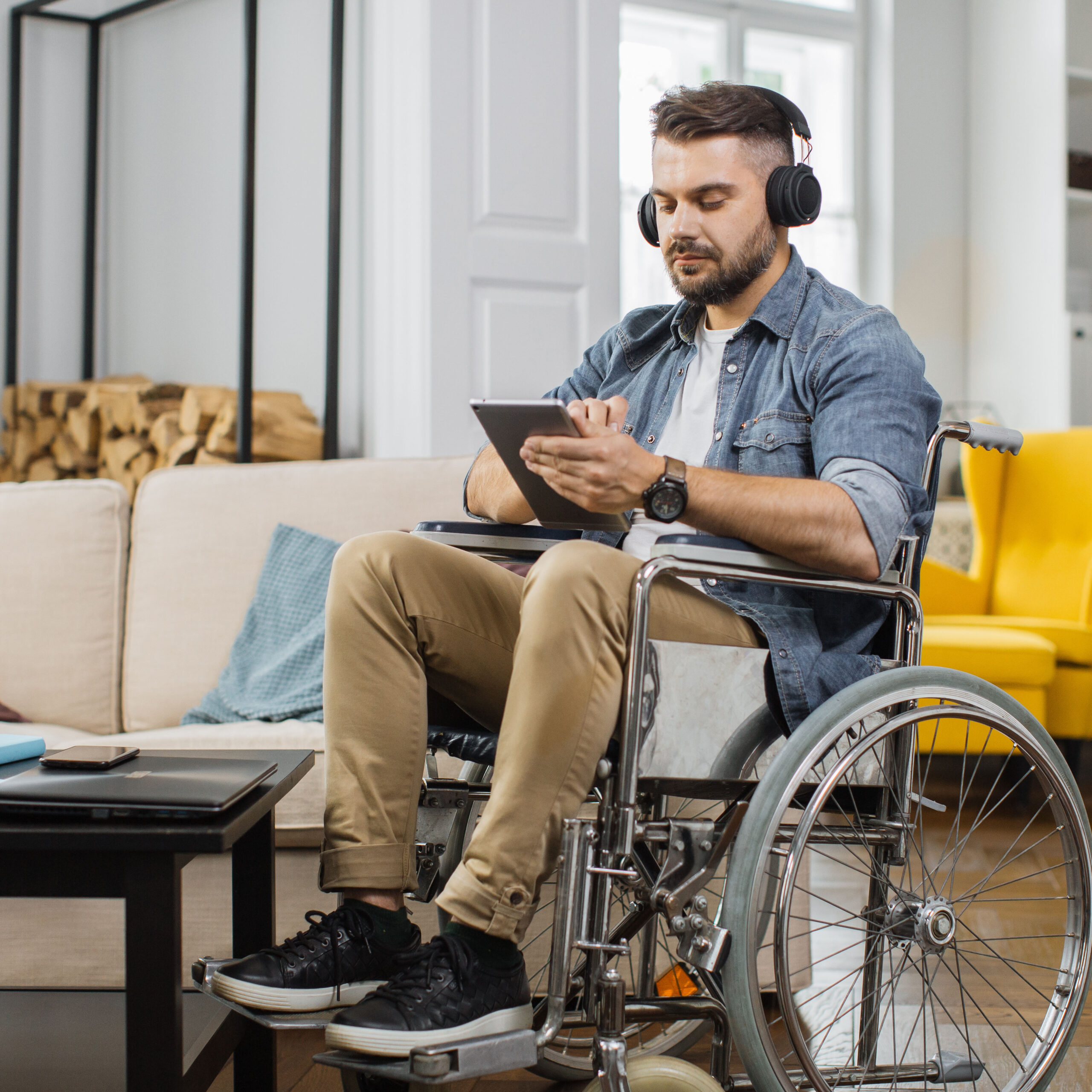 A man in a wheelchair holds an iPad in his hands while listening with headphones