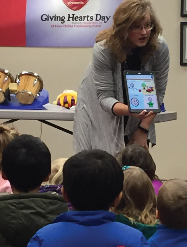 Assistive Technology Consultant Jeannie Krull holds an iPad with a communication app. She is demonstrating how the app works to a group of preschoolers.