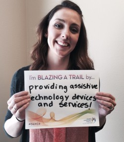 Assistive Technology Consultant Trish Floyd smiling and holding a sight that reads, "I'm blazing a trail by providing assistive technology devices and services!"
