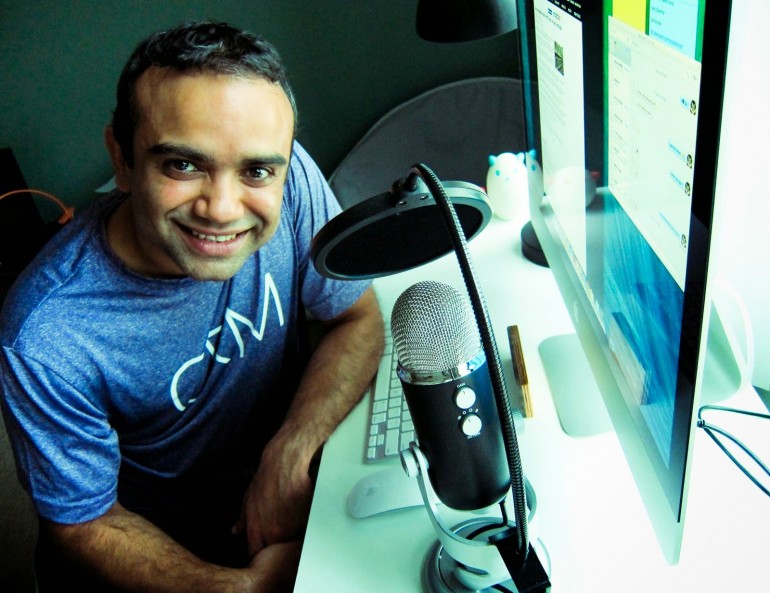 Picture of AT Blog Author Venkat Rao. He is sitting at his desk next to a microphone smiling at the camera. 