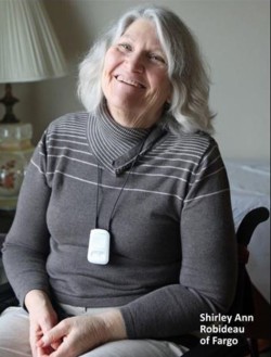 Picture of Shirley sitting in a chair smiling. She has grey shoulder length hair and is wearing a dark grey sweater.