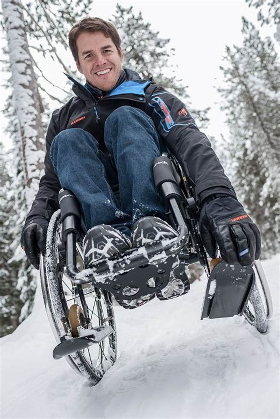 Picture of a man using a manual wheelchair with wheelblades installed in an outdoor setting with snow covered ground and evergeens.
