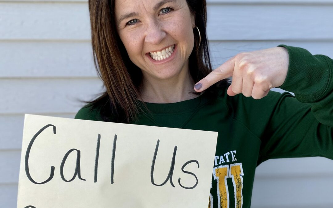 Smiling Tami Ternes pointing to a sign she is holding that says call us 800-895-4728