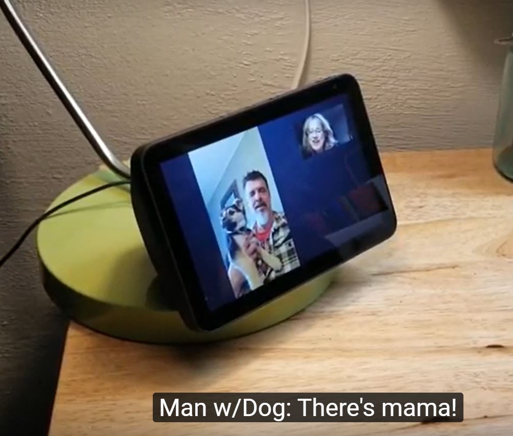 The Echo SHow with two people and a dog having a video call The captions read" Man w/Dog: "There's mama!"