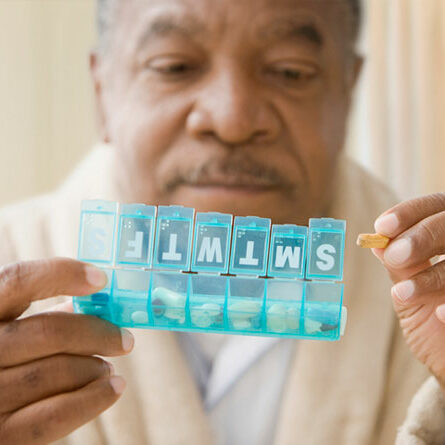 Man holding pill box with a pill in his hand.