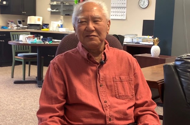 Man looking at camera.  He has gray hair and a semi-smile. Sitting in ND Assistive's demonstration center in Fargo