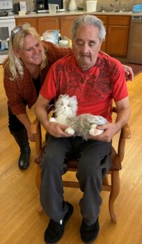 Leo Lenior is pictured seated with a robotic companion cat that he received through an ND Assistive Possibilities Grant. Leo is wearing a red t-shirt and dark pants.