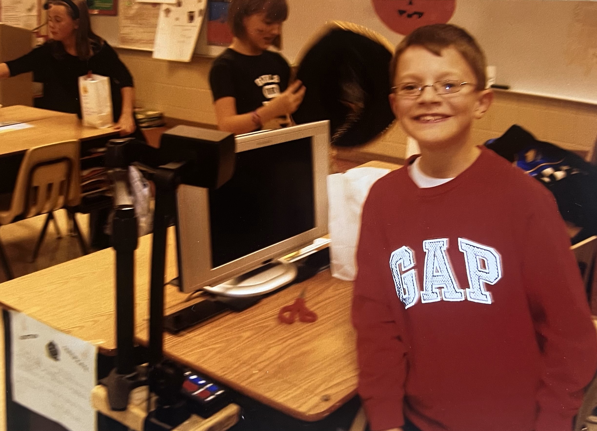 Paxton Franke as an elementary student smiling by his desk with a magnifier.